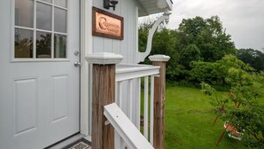 Un bâtiment blanc doté d’un porche, d’une terrasse en bois et d’une enseigne indiquant « Coppersmith Cottage ».