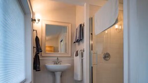 Une salle de bain avec un lavabo sur colonne, un miroir, une douche avec une porte en verre et une fenêtre.