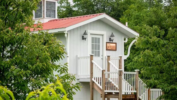 Une maison en bois blanche, avec un toit rouge, un porche à l’avant et un escalier menant à une terrasse.