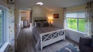 Une chambre à coucher avec un lit, une table de chevet, une lampe, une fenêtre avec des rideaux et une vue sur la verdure à l’extérieur.