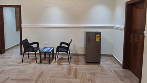 A room with a herringbone-patterned wooden floor, a small table with chairs, a refrigerator, and a door. - Cozy 1-bedroom apartment in perfect Greater Accra with AC, Fibre Internet (Greater Accra)