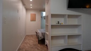 A narrow hallway with a carpeted floor, a wooden table with chess pieces, a white shelving unit, and a mounted television.