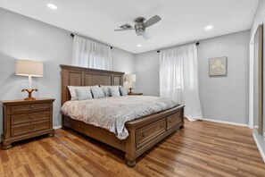 A bedroom with a wooden bed, two bedside tables, a ceiling fan, and a window with white curtains.