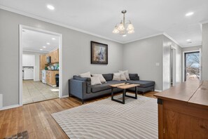 A modern living room with a grey sofa, a wooden coffee table, and a kitchen in the background.