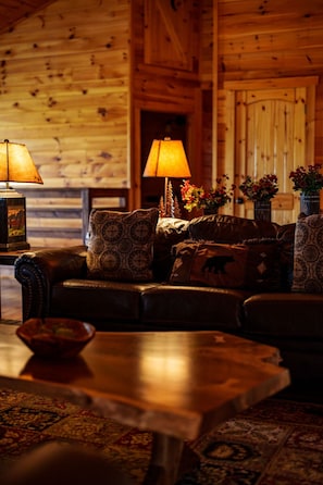 L’intérieur d’un chalet confortable, avec des murs en bois, un canapé en cuir, des coussins à motifs, une table basse en bois et deux lampes.