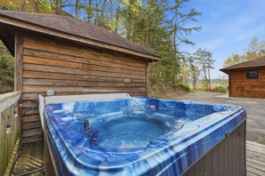 A hot tub adjacent to a wooden cabin with a clear view of the surrounding trees. - Relaxing Cabin: Views, Hot Tub, Theater, Games! (Pigeon Forge)