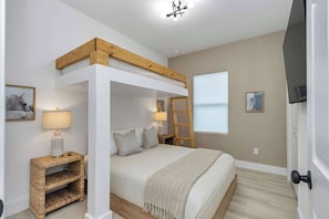 A bunk bed with a wooden frame, a bedside table with a lamp, a ladder, and a framed picture on the wall.