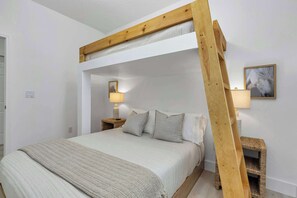 A bunk bed with a wooden ladder, a bedside table with a lamp, and a framed picture on the wall.