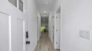 Un passadís amb portes blanques, terra de fusta, il·luminació empotrada i una zona de menjador a la distància.