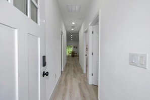A hallway with white doors, a wooden floor, recessed lighting, and a dining area in the distance.