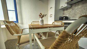 Una cocina moderna con comedor, sillas de mimbre, una mesa blanca y un jarrón con flores secas.