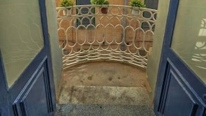 Un pasillo estrecho con barandilla de metal, un pequeño balcón con plantas en macetas y un edificio de paredes de ladrillo y ventanas.