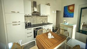 Una cocina moderna con armarios blancos, una mesa de comedor de madera, sillas de mimbre y un cuadro abstracto y colorido en la pared.