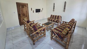 Ein Wohnzimmer mit einer Holz-Sofagarnitur, einem Couchtisch, einem an der Wand montierten Fernseher und einem Deckenventilator.
