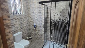 Ein Badezimmer mit Dusche, Toilette und einem Fenster mit dekorativem Gitter.