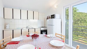Una cocina moderna con armarios blancos, un refrigerador y una mesa de comedor para dos personas, preparada con platos, vasos y un tazón de fruta.