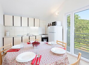 A modern kitchen with white cabinets, a refrigerator, and a dining table set for two with plates, glasses, and a bowl of fruit. - Villa Roza Dalmatian Escape (Tucepi)
