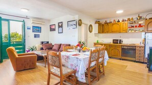 Un comedor con una mesa preparada para cuatro, sillas de madera, un sofá y una cocina con armarios y electrodomésticos de madera.