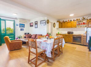 A dining area with a table set for four, wooden chairs, a sofa, and a kitchen with wooden cabinets and appliances. - Villa Roza Dalmatian Escape (Tucepi)