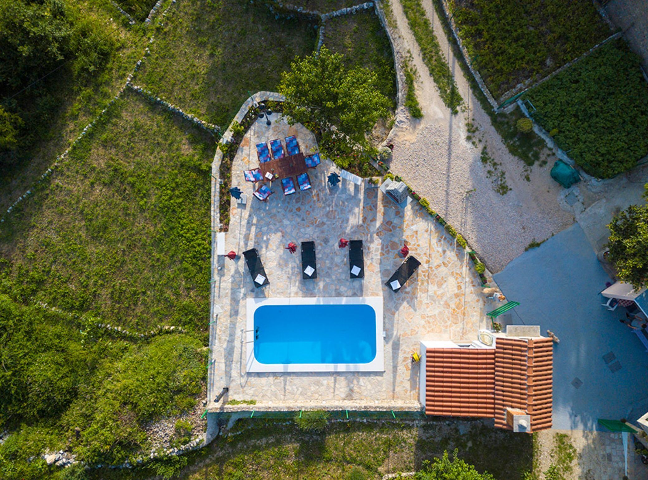 An aerial view of a pool area with lounge chairs, a swimming pool, and a tiled deck.