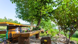 Un entorno rústico al aire libre con un banco de madera, un camino de piedra y una pequeña construcción de madera.