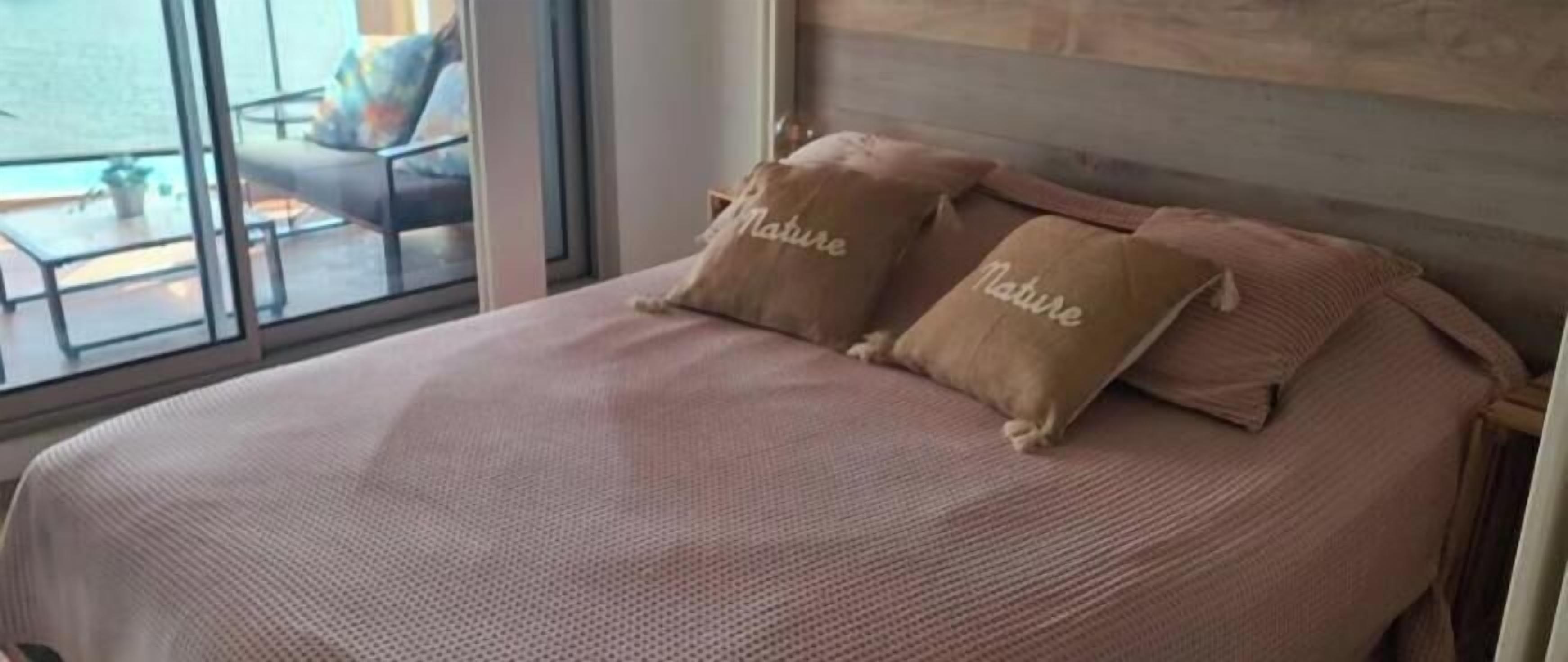 Un lit avec deux oreillers étiquetés « Nature » et une vue sur un espace extérieur aménagé, visible à travers une fenêtre.