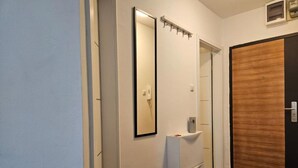 A hallway with a white wall, a wooden door, a white cabinet, and a mirror. - Apartman Fitt (Zagreb)