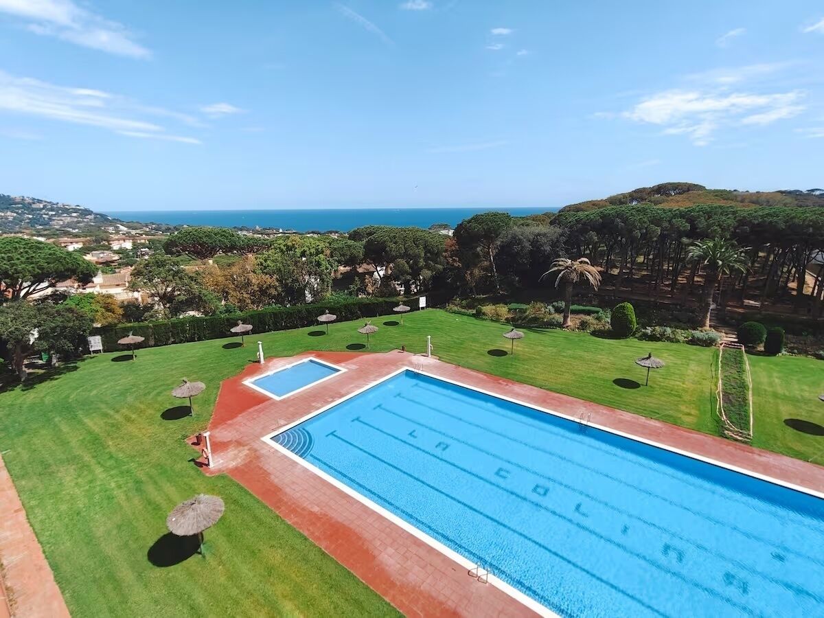 Piscina com vista para o mar, rodeada por relva bem cuidada e árvores.
