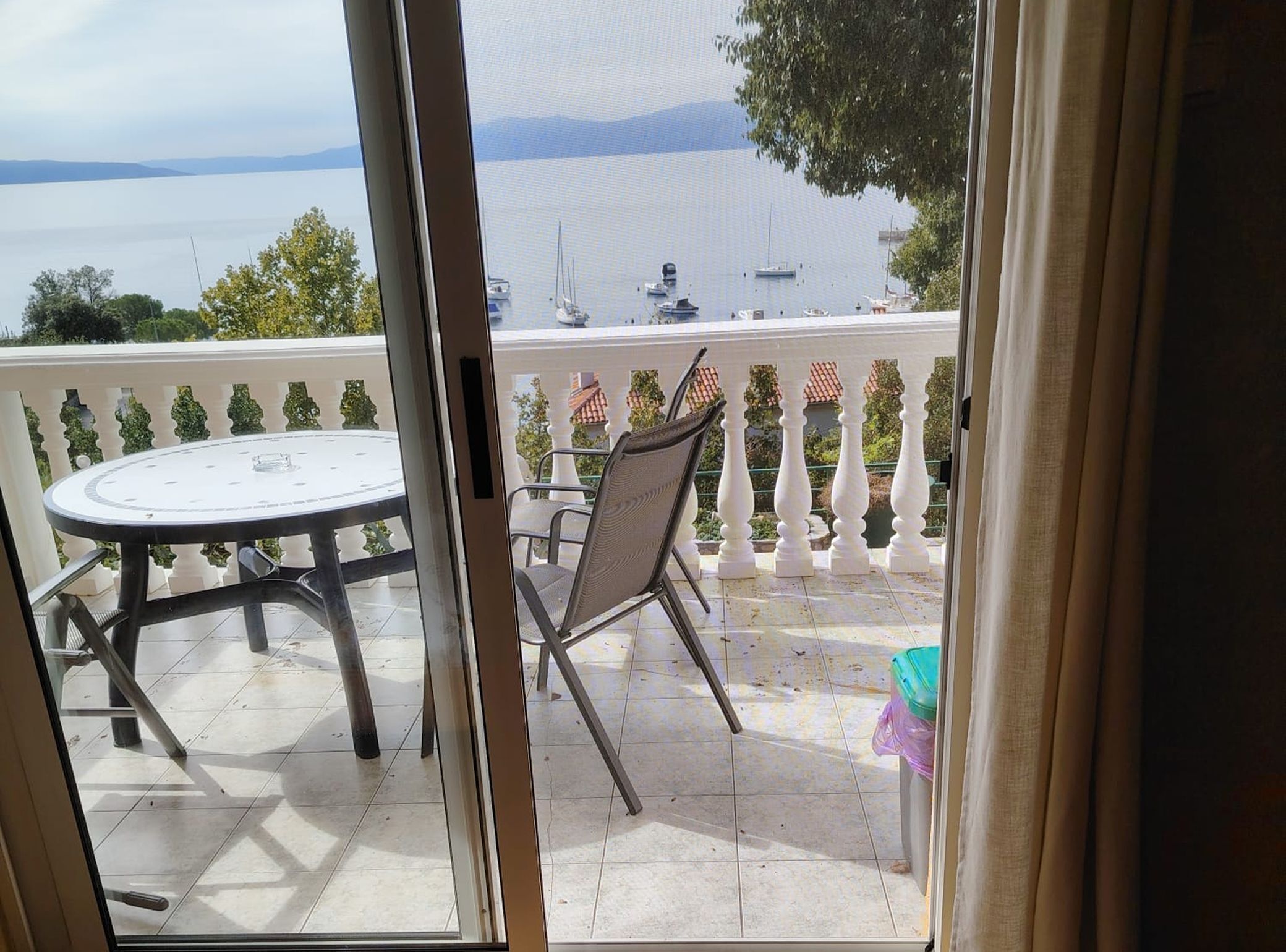 A balcony with a table and chairs, overlooking a body of water with boats.