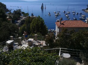 Un pueblo costero con un puerto deportivo, edificios de piedra y un velero destacando en la distancia.