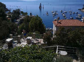 Un pueblo costero con un puerto deportivo, edificios de piedra y un velero destacando en la distancia.