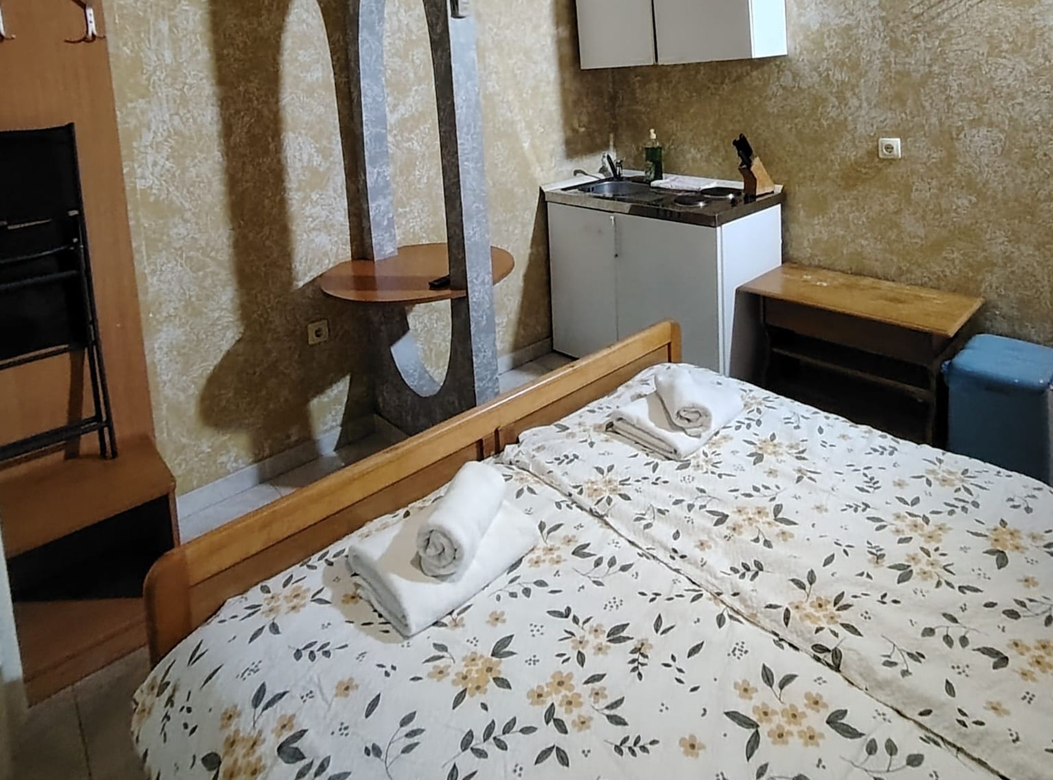 A bedroom with a bed, a wooden nightstand, a small table, and a wardrobe.