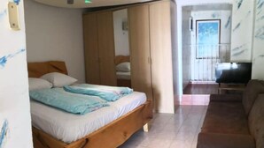 A bedroom with a wooden bed, a wardrobe, and a television in the adjacent living area. - Comfort Kostrena Apartments Rijeka (Kostrena)
