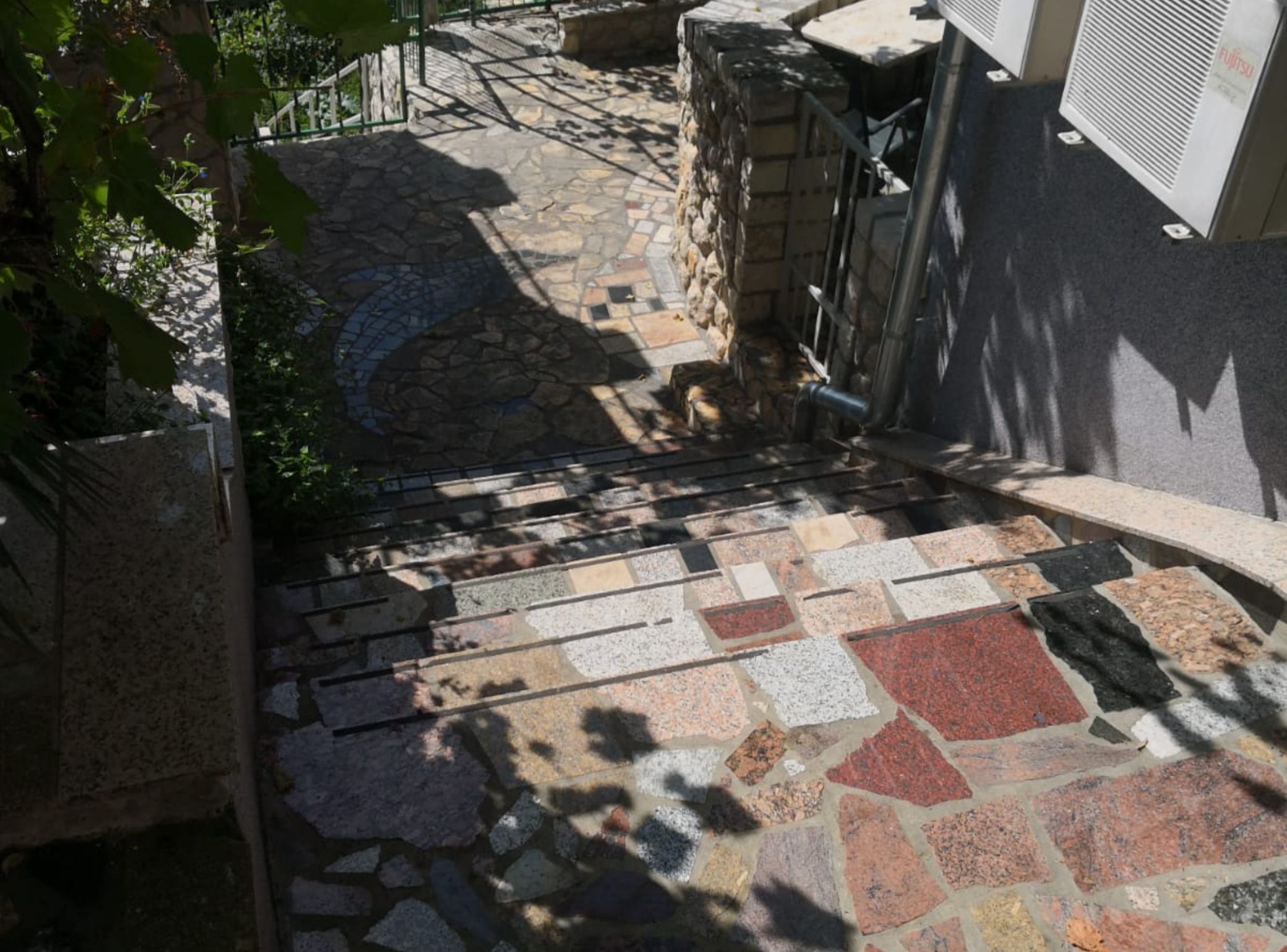 A stone staircase leading to a building entrance, surrounded by greenery and stone walls.