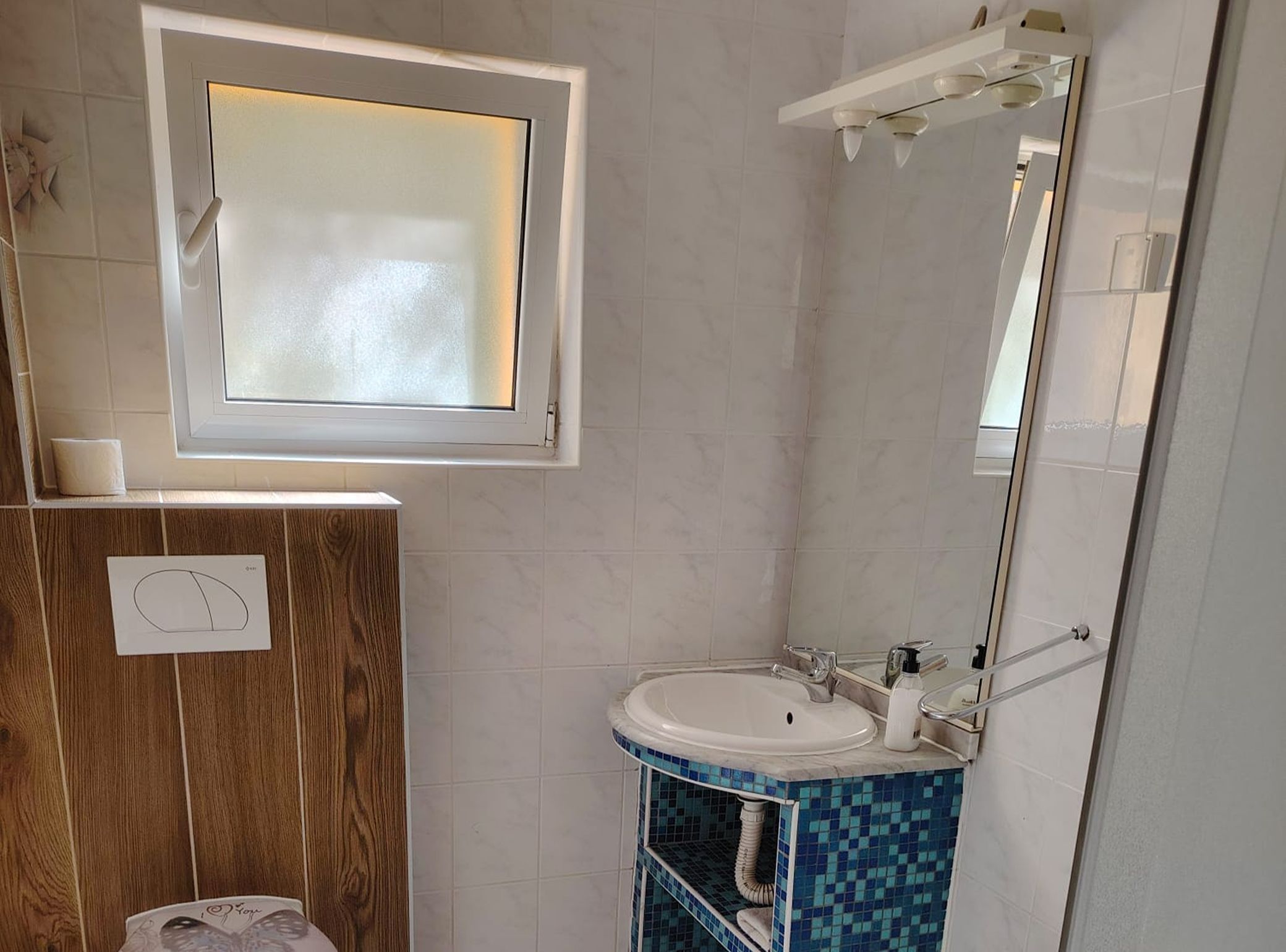 Un baño con tocador de madera, un lavabo blanco, un espejo y un ventanal sobre el tocador.