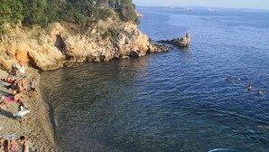 A coastal beach with rocky terrain, clear water, and a few people swimming. - Comfort Kostrena Apartments Rijeka (Kostrena)