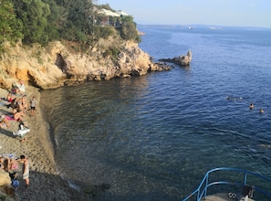 Una playa costera con terreno rocoso, agua cristalina y algunas personas nadando.