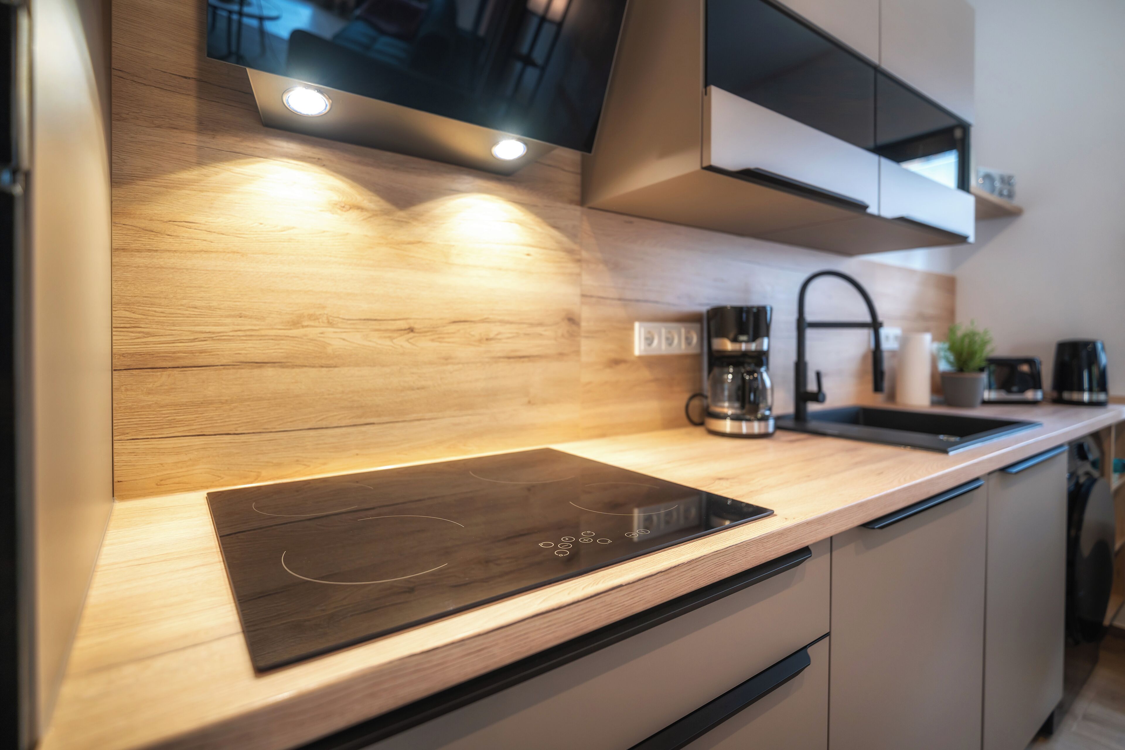 A modern kitchen with a wooden countertop, a built-in induction cooktop, a coffee maker, and a microwave.
