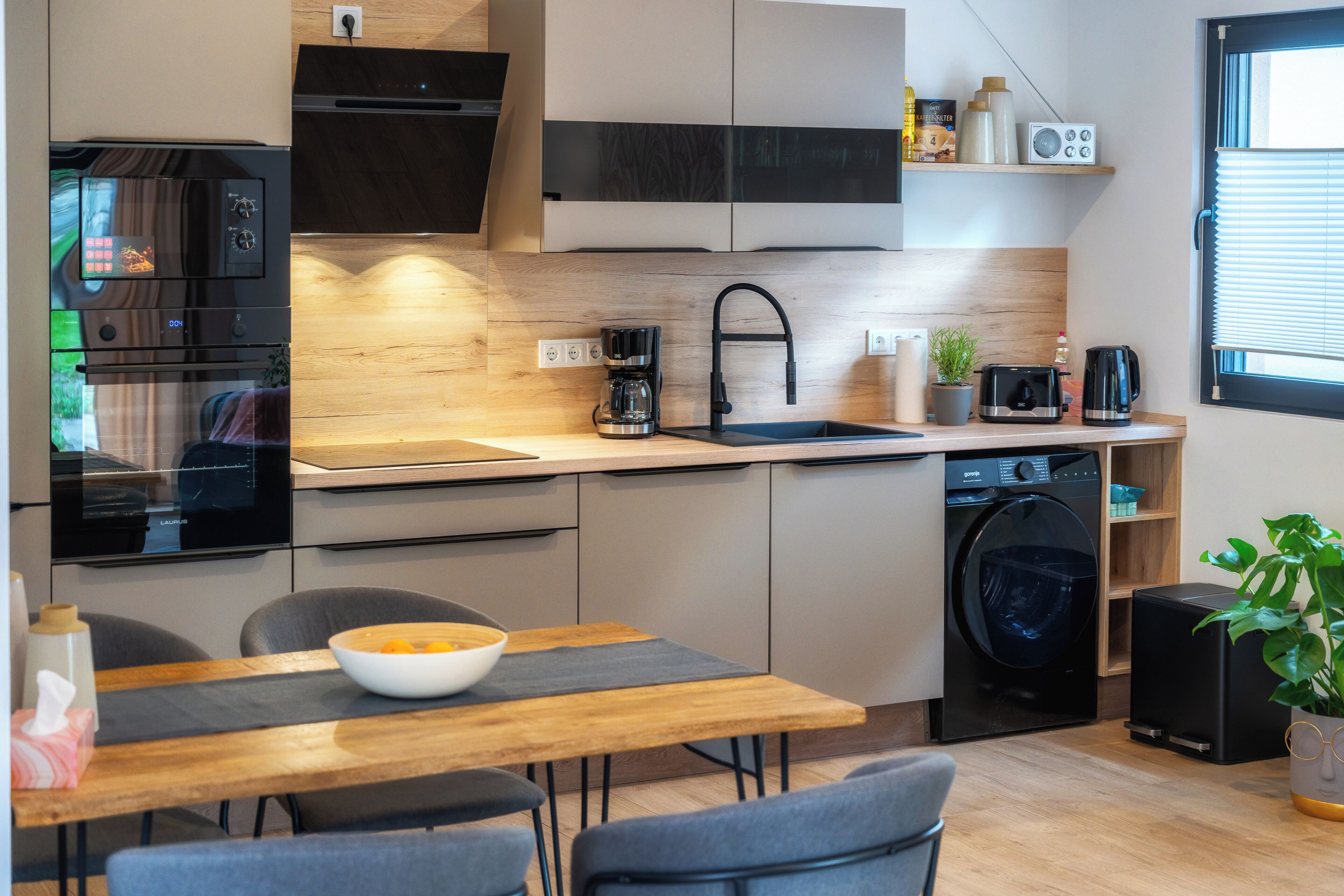 Eine moderne Küche mit Backofen, Kaffeemaschine, Spüle und Waschmaschine.