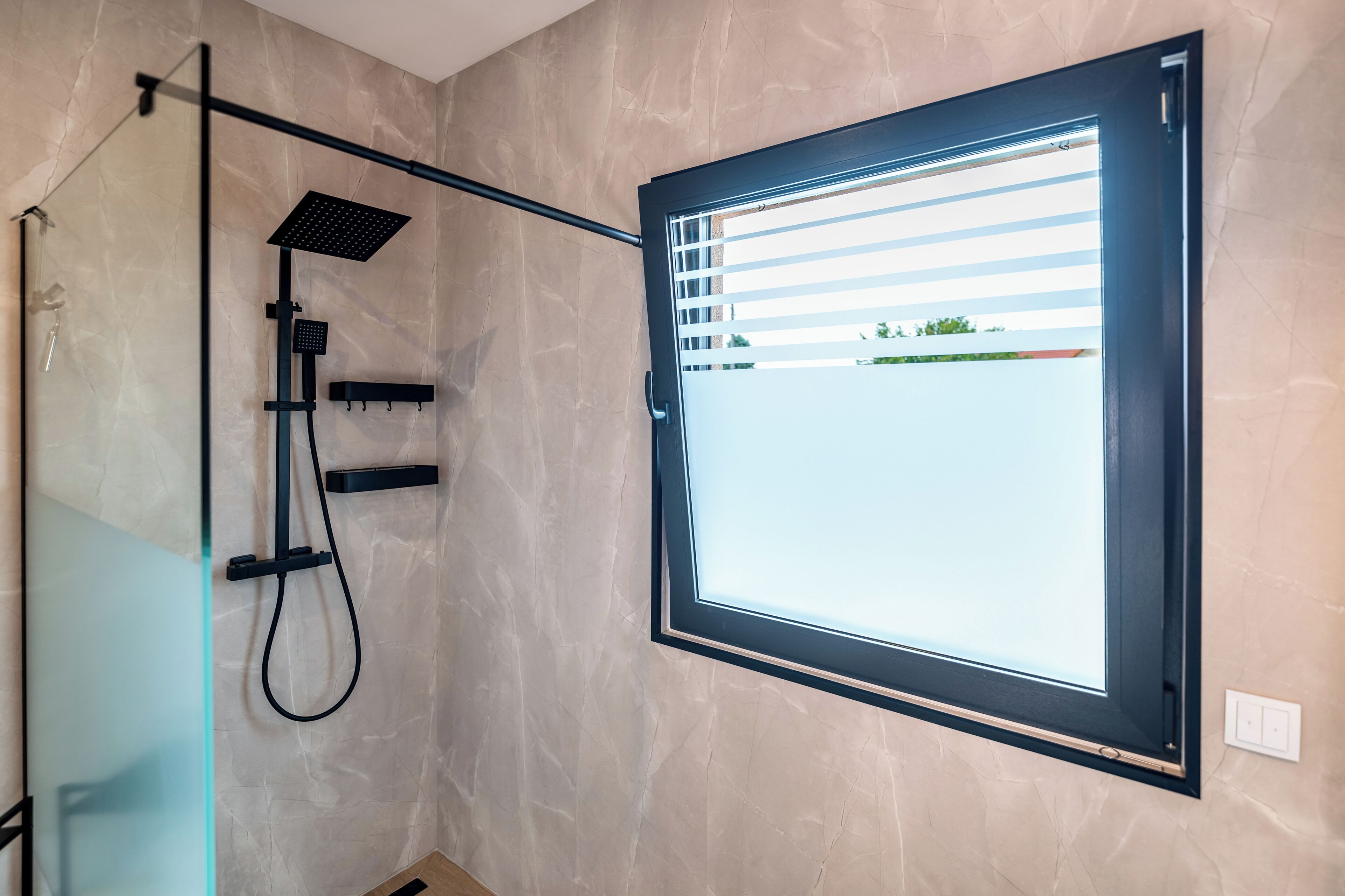 Ein modernes Badezimmer mit Duschkabine aus Glas, integriertem Fenster und Blick ins Freie.