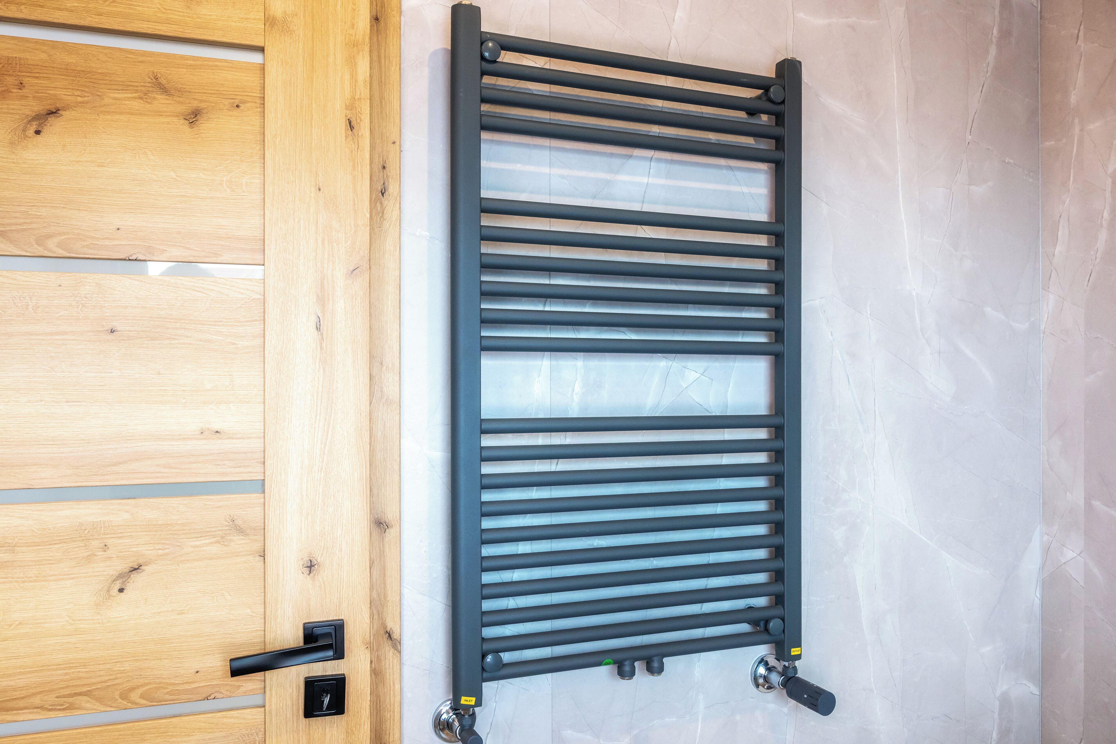 A bathroom with a wooden door, a black towel rack, and a white tiled wall.
