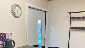 A dining area with a table, chairs, a clock, and a door leading outside. - Wimbleball Lake View Cabin Sleeps up to 3 (Dulverton)
