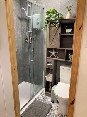 A shower with a glass door, a toilet, a sink, and a wooden shelf with plants and decorative items. - Wimbleball Lake View Cabin Sleeps up to 3 (Dulverton)