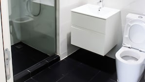 A modern bathroom with a glass-enclosed shower, a white sink, and a toilet. - Embassy Gardens Exquisite (Accra)