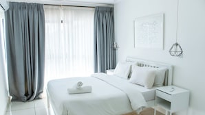 A modern hotel room with a neatly made bed, a bedside table with a phone, and a window with grey curtains. - Embassy Gardens Exquisite (Accra)