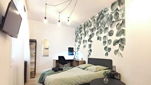 Une chambre à coucher comprenant un lit, un bureau, une chaise, une table ronde et un téléviseur fixé au mur.