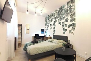Une chambre à coucher comprenant un lit, un bureau, une chaise, une table ronde et un téléviseur fixé au mur.