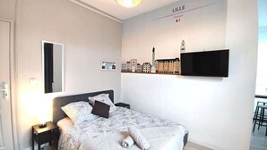 Ein Hotelzimmer mit einem Bett, einem an der Wand befestigten Flachbildfernseher, einem kleinen Tisch mit einer Lampe und einem Stadtbild-Wandgemälde.