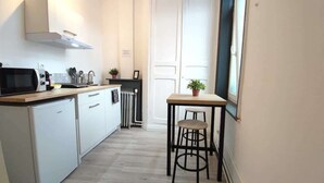 Eine kleine Küche mit Mikrowelle, Spüle und Schränken, ein Tisch mit einem Hocker und ein Heizkörper.