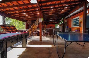 A covered outdoor area with a ping pong table, a pool table, and a hammock.